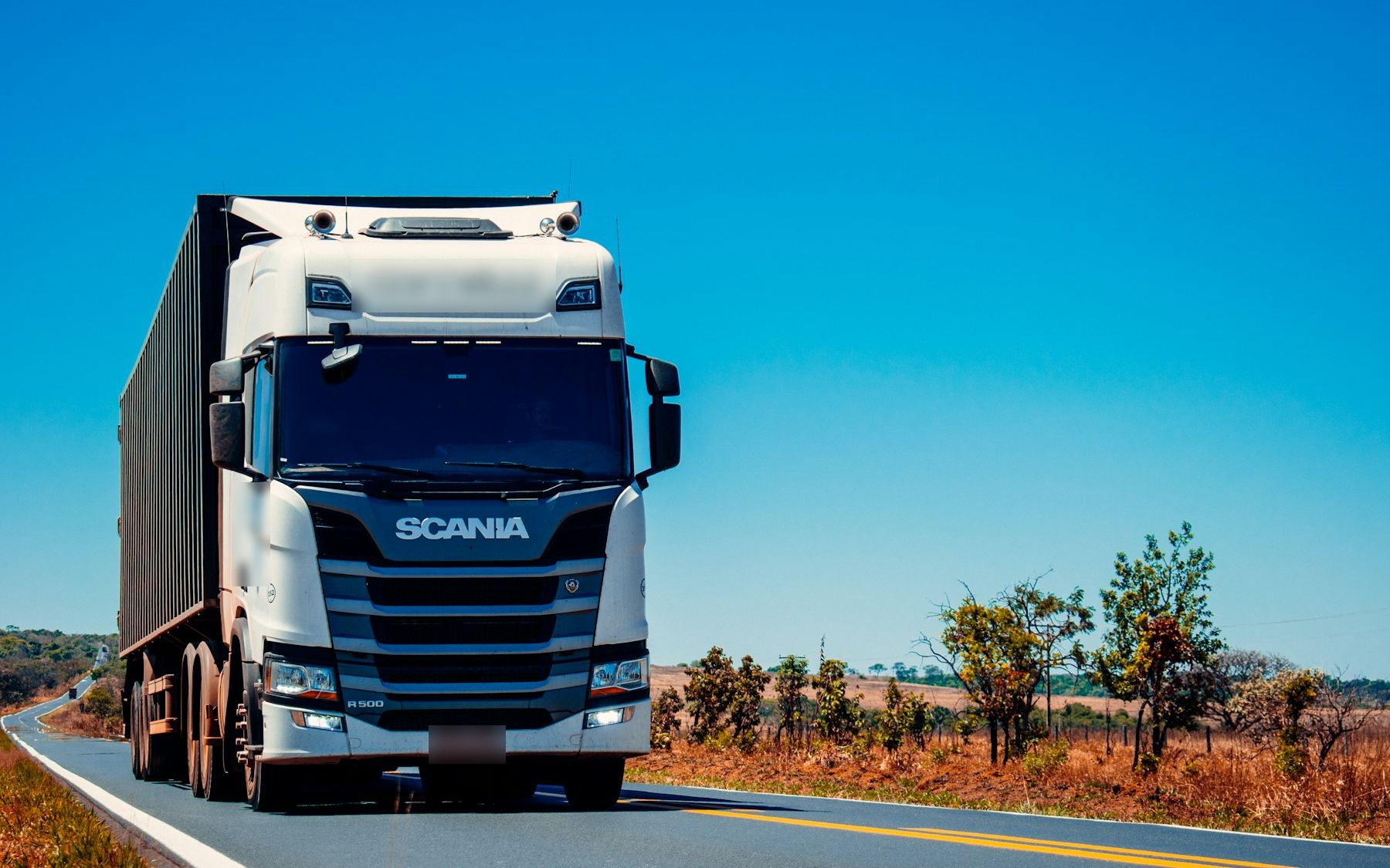 Scania-dragbil med trailer på landsväg i solsken